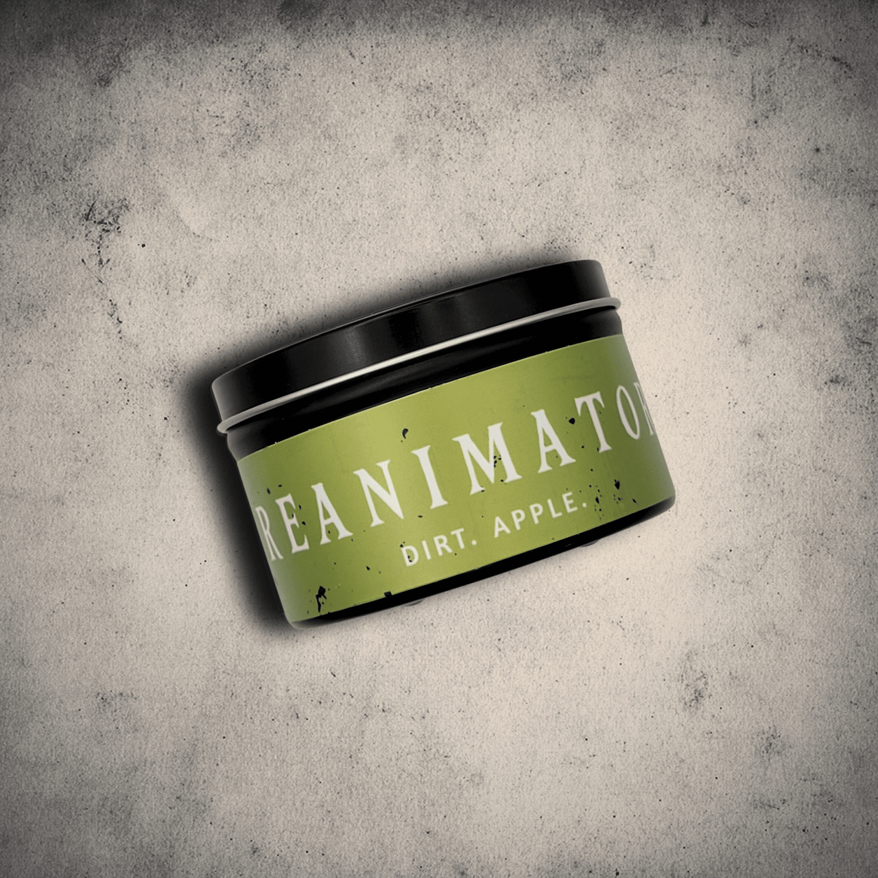 Emberlight Archives Reanimator candle in an 8oz black tin with bright green label against a gray stone background, Dirt and Apple scent.